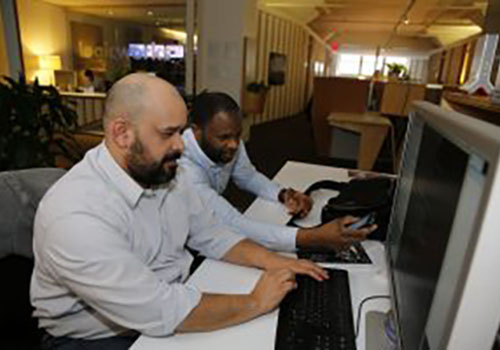 Two men sitting at a desk looking at a computer monitor